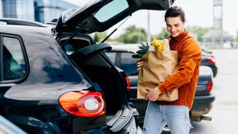 Ein junger Mann hebt eine Papiertüte mit Lebensmitteln aus dem Kofferraum seines Autos beim REWE Abholservice.