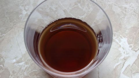 Ein Glas mit einer dunklen Flüssigkeit steht auf einer hellen, marmorierten Oberfläche. Es könnte als Lockmittel für lästige Obstfliegen dienen.