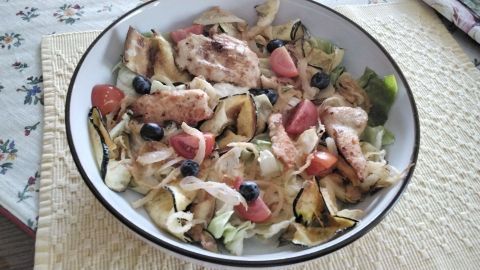 Gestreifte Putenstücke liegen auf einem frischen Salatbett mit Tomaten und Gemüse, umgeben von einem gedeckten Tisch.