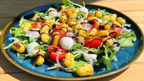 Gnocchi liegen dekorativ auf Rucola, Tomaten und Zwiebeln, angerichtet auf einem blauen Teller auf Holztisch.