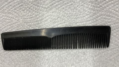 Dein Kamm sollte regelmäßig von Schmutz und Stylingrückstände befreit werden. Ein schwarzer Kamm liegt auf einem weißen Tuch, bereit zur Reinigung von Schmutz und Stylingrückständen.