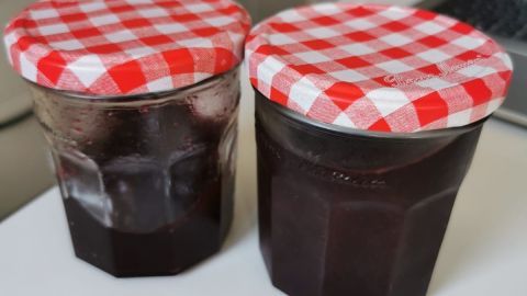 Zwei Marmeladengläser mit rot-weiß karierten Deckeln stehen auf einem weißen Tisch in einer modernen Küche.