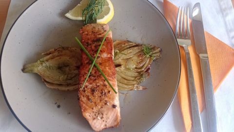 Gegrillter Lachs liegt auf gebratenem Fenchel, begleitet von einem Salat und würzig gewürfelten Kartoffeln in Schalen.