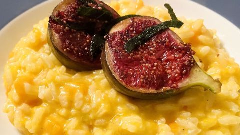Risotto mit Butternut-Kürbis, garniert mit frischen Feigen und frittiertem Salbei, serviert auf einem weißen Teller.