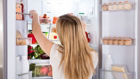 Frau organisiert Kühlschrank, arrangiert Lebensmittel und Getränke, um mehr Ordnung im Innenraum zu schaffen.