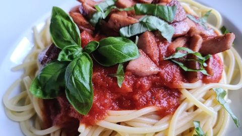 Spaghetti mit Tomatensoße und Basilikum werden auf einem Teller serviert, garniert mit geschnittenen Pilzen und frischem Basilikum.