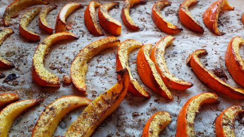 Kürbis-Pommes liegen geröstet auf einem Backblech in der Küche, umgeben von Kräutern und Gewürzen auf Backpapier.