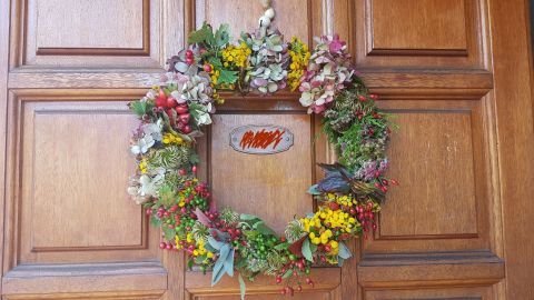 Ein Herbstkranz aus bunten Trockenblumen und Beeren hängt dekorativ an einer Holztür.