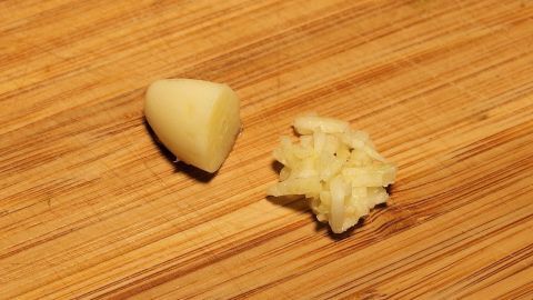 Ein Knoblauchzehe liegt neben zerdrücktem Knoblauch auf einem Holzbrett, optimal zur Bekämpfung von Fußpilz und Nagelpilz.