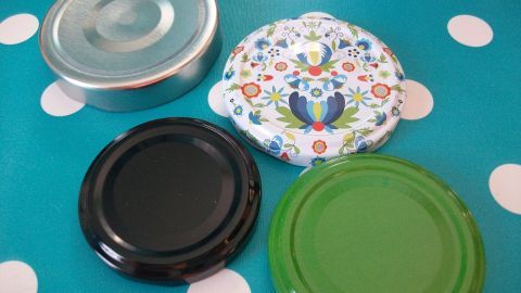 Verschiedene Ersatzdeckel für Twist-Off-Gläser liegen auf einem blau-weiß gepunkteten Untergrund.