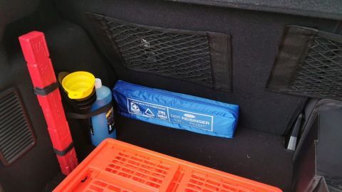 Kofferraum mit sorgfältig organisiertem Zubehör: blaues Erste-Hilfe-Set, rote Klappbox, Frostschutz, Warndreieck und gelber Trichter.