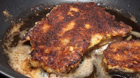 Zwei scharfe, goldbraun panierte Schweineschnitzel brutzeln in einer heißen Pfanne mit zischendem Fett.