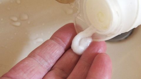 Eine Hand hält eine flüssige Spülung, die aus einer Flasche fließt, während sie über einem Waschbecken steht.