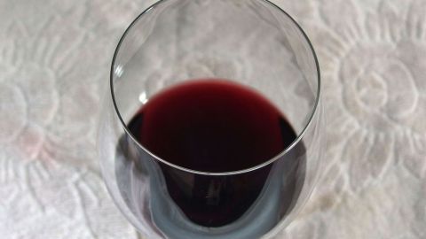 Ein Rotweinglas steht auf einem eleganten, weiß gemusterten Tischcloth. Der dunkle Wein reflektiert das Licht.