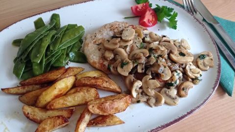 Genieße ein klassisches Jägerschnitzel mit Pilzrahmsoße, deftigen Kartoffeln und frischem Gemüse. Perfekt für ein herzhaftes Abendessen.