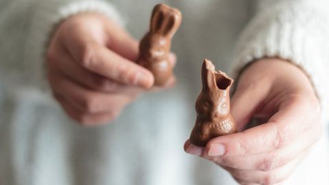 Kinderhände halten zwei Schokoosterhasen. Einem wurden bereits die Ohren abgebissen. 