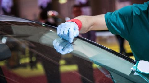 Ein Handwerker reinigt mit einem Tuch eine Autoscheibe gründlich, um Schmierflecken zu entfernen, während andere zuschauen.