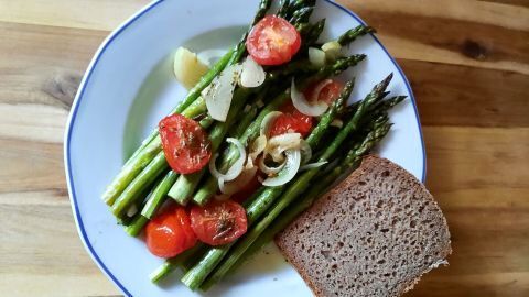 Grüner Spargel mit Tomaten und Zwiebeln aus dem Backofen, serviert mit Brot – so einfach und lecker sieht das im Rezept aus.