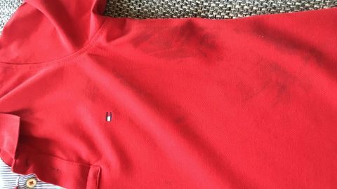 Ein rotes Kleidungsstück liegt auf einem grauen, strukturierten Untergrund mit sichtbaren Fettflecken.