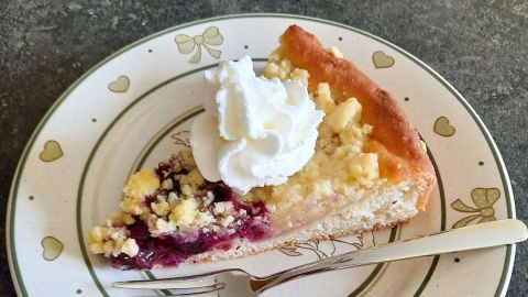 Mit einem Klecks Schlagsahne sieht der Fächer-Apfelkuchen mit Heidelbeeren und Streuseln noch leckerer aus.