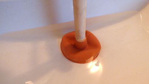 Ein Pümpel steht in einem Waschbecken und wird verwendet, um das Wasser abzusaugen und eine Verstopfung zu lösen.