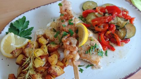 In der Pfanne gebratener Kabeljau mit Kartoffel- und Gemüsebeilage. Das Fischfilet wird noch mit dem kurz gebratenen Garnelen-Spieß belegt.