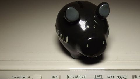 Das schwarze Sparschwein steht auf einer Waschmaschine und symbolisiert extra-Haushaltsgeld beim Waschen.