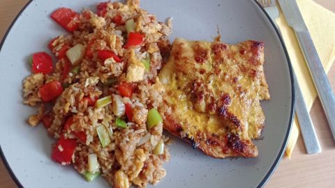 Das gebratene Putenfilet mit der würzigen Gemüse-Reis-Pfanne wird auf vorgewärmten Tellern angerichtet.