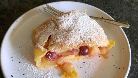 Ein gelungenes Stück des Zwetschgenstrudels mit Apfel und Trauben. Der obere Teig ist knusprig, mit einem Hauch Puderzucker.