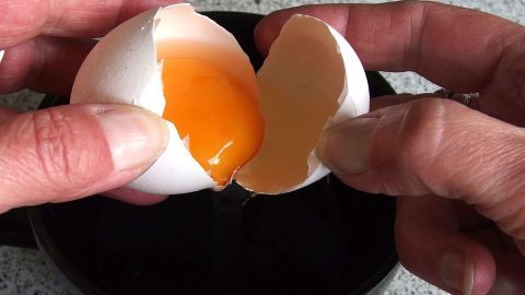 Eine Hand hält ein aufgeschlagenes Ei über eine Schüssel, während der Dotter vorsichtig herausgenommen wird.