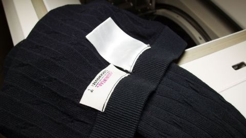 Schwarze Strickmütze liegt auf einer Waschmaschine, bereit zum Linksrum waschen. Pflegeetikett ist sichtbar.