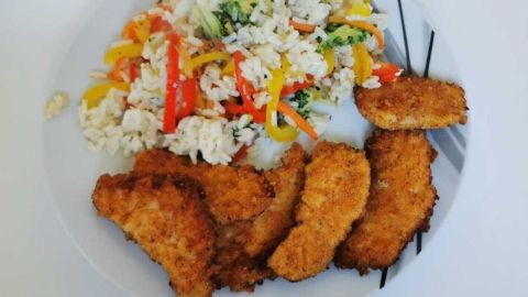 Selbstgemachte scharfe H&auml;hnchen-Nuggets mit Reis und frischem Gem&uuml;se serviert auf dem Teller.