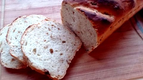 Zwiebelbrot nach dem Rezept: goldbrauner Laib mit eingeschnittenem Muster, dazu luftige Scheiben auf dem Schneidebrett.