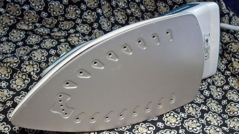 Ein B&uuml;geleisen liegt auf einem gemusterten Stoff und ist bereit, um gereinigt zu werden, was die Pflege des Haushalts unterst&uuml;tzt.