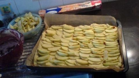 Ein frisch zubereiteter Apfelkuchen liegt in einer Backform, mit gleichmäßig geschnittenen Äpfeln belegt, auf einer Küchentheke.