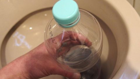 Eine Plastikflasche wird benutzt, um ein verstopftes Klo zu reinigen. Die Flasche ist teilweise im Toilettenbecken.