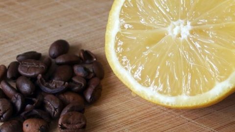 Eine halbierte Zitrone liegt neben einer Menge gerösteter Kaffeebohnen auf einem Holzbrett, was auf mögliche Mittel gegen Kopfschmerzen hindeutet.