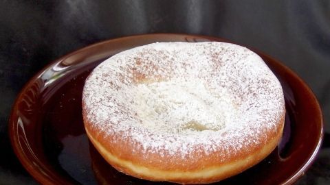 Ein runder, feinporiger Hefeteig ist auf einem braunen Teller angerichtet, mit Puderzucker bestäubt, und hebt sich vor einem dunklen Hintergrund ab.