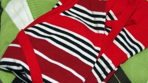 Ein gestreiftes rotes Kleidungsstück liegt zusammen mit grüner und schwarzer Kleidung auf einem Haufen.