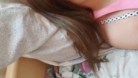 Ein Haarsträhne mit Grünstich vom Haarefärben liegt auf einem Bett mit gemusterten Kissen und Decke, neben einer Person.