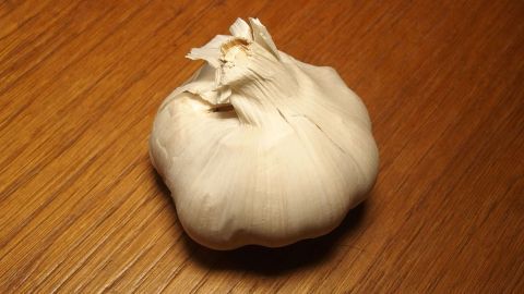 Eine Knoblauchknolle liegt auf einem holzfarbenen Tisch und wartet darauf, zur Zubereitung von Gerichten verwendet zu werden.