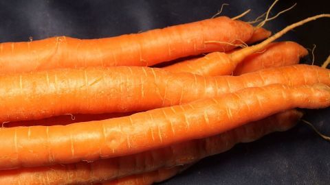 Frische, orange Möhren liegen übereinander auf einem dunklen Untergrund und vermitteln eine appetitliche Ausstrahlung.