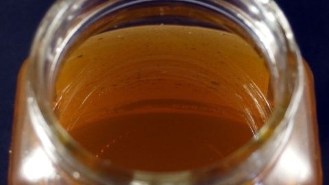 Ein Glas Honig steht auf einem Tisch. Der goldene Honig schimmert im Glas, das Licht reflektiert die samtige Oberfläche im Raum.