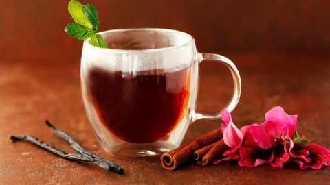 Ein Glas Tee steht auf einem Rustikalen Tisch, umgeben von Zimtstangen und Blumen, der Duft weckt Schokohunger.