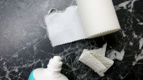 Eine Tube Sole-Zahncreme steht auf einer dunklen Marmoroberfläche, daneben liegen Streifen eines weißen Pflasters.