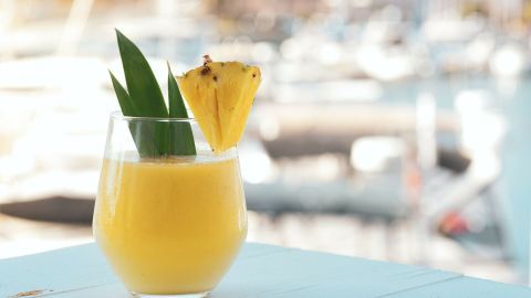 Ein leuchtend gelber alkoholfreier Pina Colada Cocktail in einem Glas steht auf einem Tisch, umgeben von einem maritimen Hintergrund.