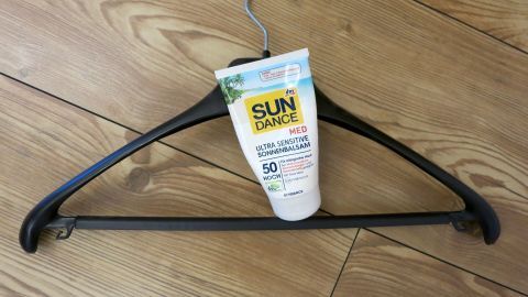 Kleiderbügel hält Sonnencreme "SUN DANCE MED Ultra Sensitive Sonnenbalsam 50 Hoch" auf Holzfußboden.