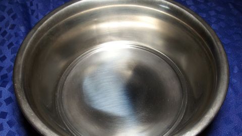 Eine glänzende Edelstahlschüssel steht auf einem blauen Tuch und reflektiert das Licht, zeigt ihre Sauberkeit und Pflege.