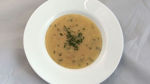 Eine cremige Suppe in einer weißen Schüssel, garniert mit frischen Kräutern, auf einem gedeckten Tisch.