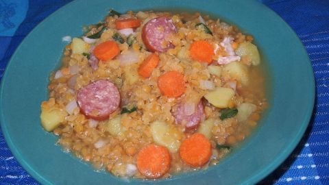 Eine schüsselweise Turbo-Linsensuppe wird serviert, voller Linsen, Karotten und Würstchen in einer herzhaften Brühe.